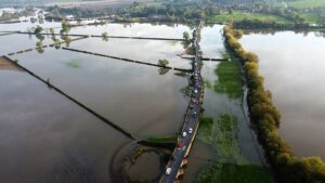An aerial photograph taken on October 24, 2023 shows vehicles travelling along the Swarkestone Bridge, in the Village of Swarkestone, in Derbyshire, as fields are flooded following the storm Babet. A fifth death was confirmed in the United Kingdom on October 23, 2023 following the torrential rains and high winds brought by Storm Babet, which caused extensive flooding across the country. (Photo by Justin TALLIS / AFP) (Photo by JUSTIN TALLIS/AFP via Getty Images)