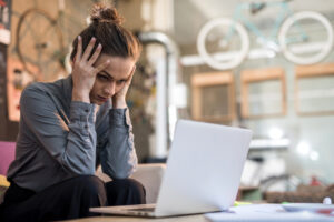 Young frustrated businesswoman working on laptop and holding her head in hands
